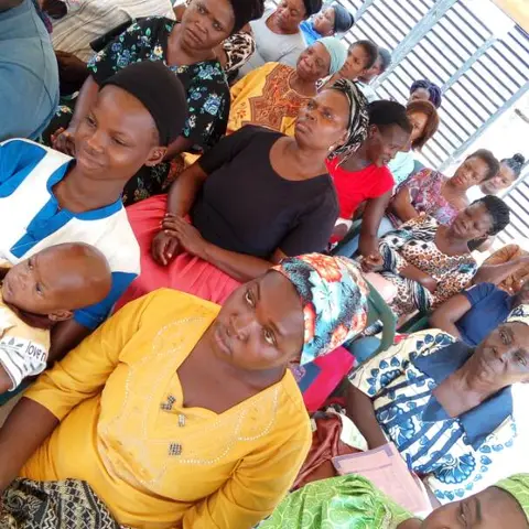 A close-up view of women crowded together in seats at an outdoor community meeting, focused on the proceedings.