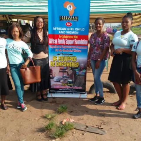 Four individuals standing in front of a Charitas Orphanage and Widowhood Foundation banner.