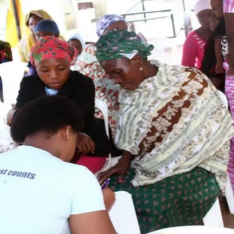 A foundation volunteer at a white table registers a community participant, with women waiting in line behind her.