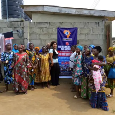 A large group photo of women and children standing beside the LFAGCW and African Family Support Foundation banner at an outdoor empowerment event in Nigeria.