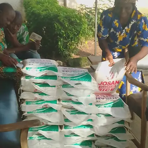 A man in a blue printed shirt sorts and stacks bags of Josan Parboiled Rice on a table in preparation for community distribution.