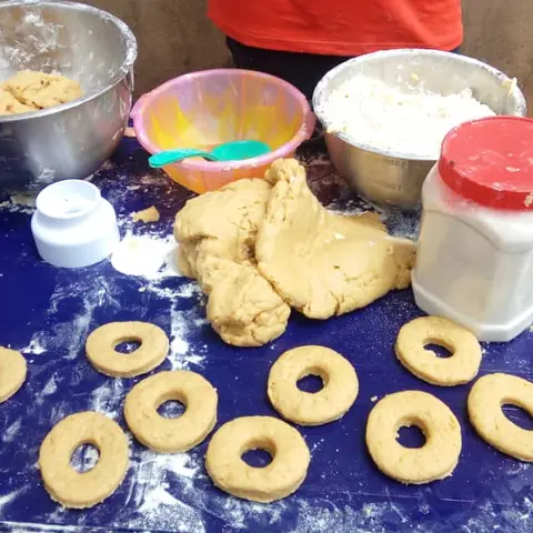 A close-up of shaped dough rings and mixing bowls with dough and flour on a blue table at a vocational baking demonstration.
