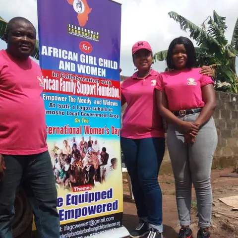Three foundation volunteers in pink shirts standing beside the 'African Girl Child and Women – Be Equipped Be Empowered' pull-up banner.