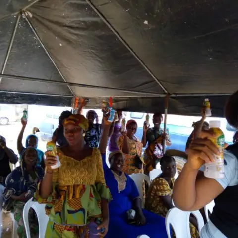 Joyful women under a canopy tent raise bottles of nutritional drinks in celebration following a successful empowerment event.