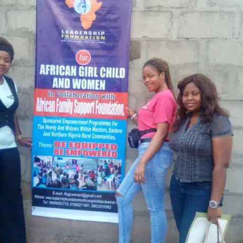 Two women posing beside the 'African Girl Child and Women – Be Equipped Be Empowered' pull-up banner at an outdoor event.