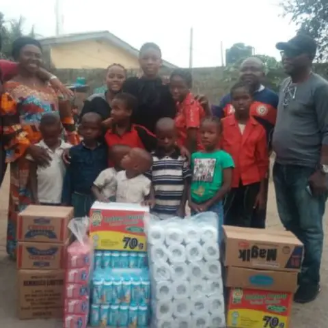Foundation volunteers and community members pose in an open area with boxes of donated food and household supplies for an outreach visit.