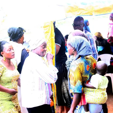 Women in colourful clothing talking and gathering under a yellow canopy tent at an outdoor community outreach event.