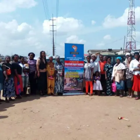 A large group of women standing in a line in front of the 'African Girl Child and Women – Be Equipped Be Empowered' banner for a group photo outdoors.