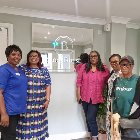 Five women standing together in the lobby of Brook House, smiling for a group photo. One woman is wearing blue medical scrubs.
