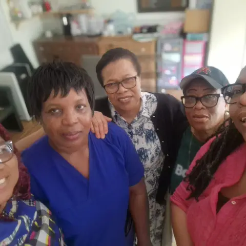 A friendly group selfie of five women smiling together indoors, likely staff or volunteers at Brook House.