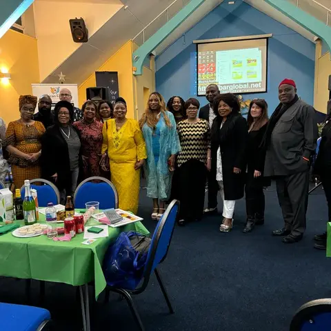 A large group of attendees and volunteers smiling for a photo in the community hall, dressed in both festive and traditional attire.