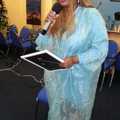 A woman in a black and gold top holding her certificate and smiling for a photo with the host.
