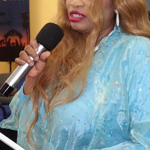Attendees standing and chatting in the community hall, with blue chairs and festive decorations visible.