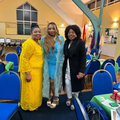 A man in a Christmas-patterned shirt speaking into a microphone, standing next to another man in a patterned shirt.