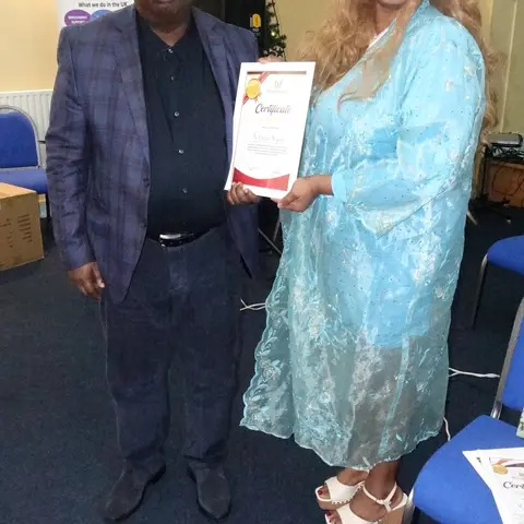 A man in a blue suit presenting a certificate of appreciation to a woman in a shimmering light blue dress.