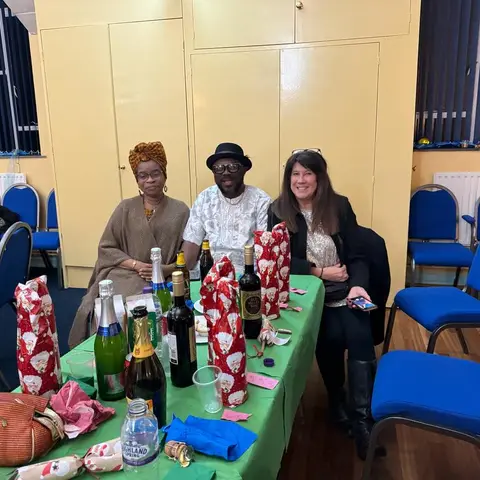A woman in a black and gold top receiving a certificate, both she and the presenter are looking at the camera.