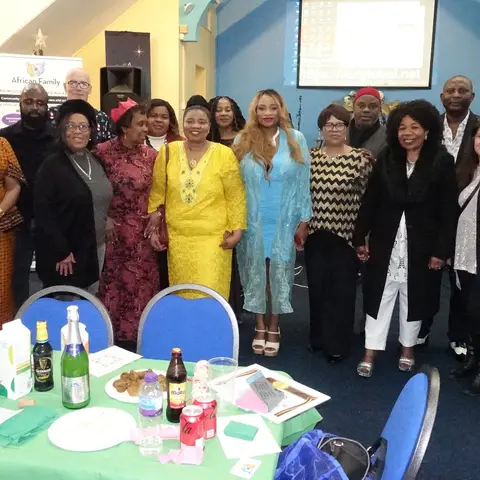 A joyful group photo of community members, some wearing festive paper hats, standing together at the Christmas party.
