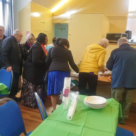Volunteers and guests gathering around the food service table to plate up their meals.