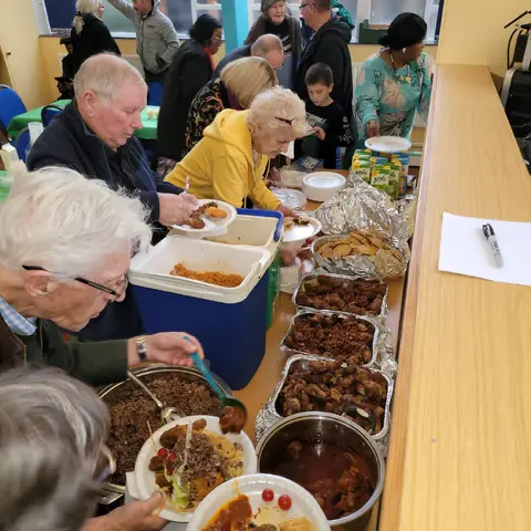 Attendees serving themselves from a buffet line featuring various dishes in large metal trays and insulated containers.