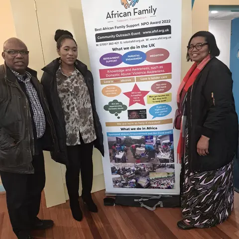 Three attendees posing for a photo beside the African Family Support Foundation information banner.