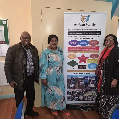 Two women and a man smiling for a photo beside the foundation's roll-up banner.