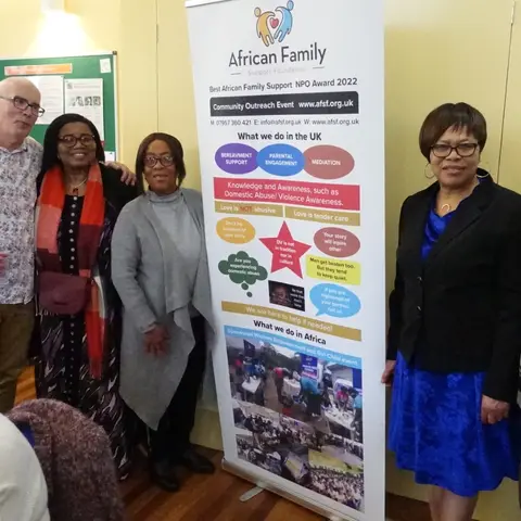 A group of four community members standing together next to the AFSF banner.