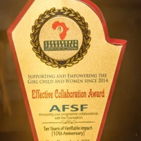 A gold and red flame-shaped award presented to AFSF by the Leadership Foundation for African Girl Child and Women for 'Effective Collaboration,' commemorating ten years of verifiable impact, dated December 1, 2024.