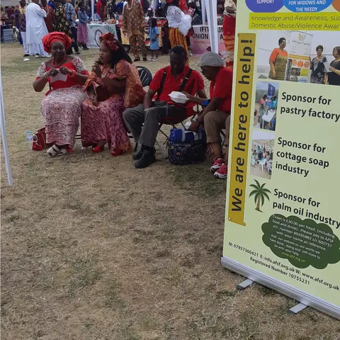Attendees in colorful traditional attire seated under a white tent at the Igbo Day Festival, next to the foundation's banner.