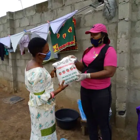 A foundation volunteer in pink hands a bag of rice to a woman in a green floral dress, with the AFSF banner visible behind them.