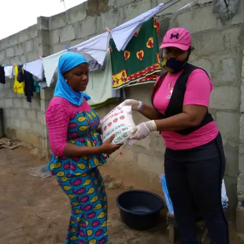 A foundation volunteer in pink hands a bag of rice to a woman in a yellow and blue kente-style dress during the food distribution programme.