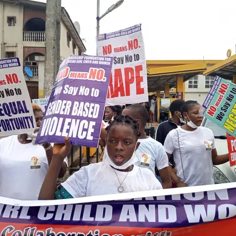 Marchers from the Leadership Foundation for African Girl Child and Women holding signs reading 'No Means No – Say No to Gender Based Violence' and 'Say No to Rape' during a street march.