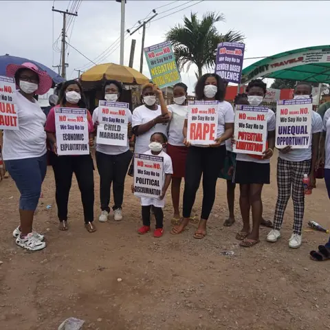 Foundation volunteers and community members wearing face masks hold placards reading 'No Means No – We Say No to Sexual Assault, Child Marriage, Rape, and Poor Education' at an outdoor march.
