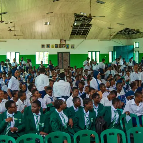 Hundreds of schoolgirls and boys in green and white uniforms seated in a large school hall for the International Day of the Girl Child event.