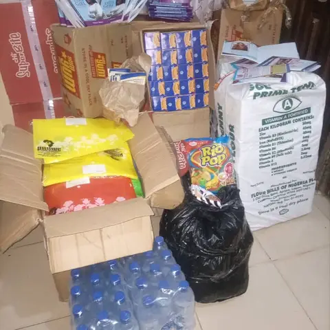 Supplies prepared for the Girl Child Day event, including boxes of food, bags of flour, books titled 'A Super Girl Approaches,' and bottles of water.
