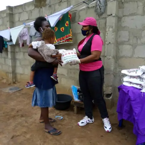 A man and two women in pink shirts standing next to a promotional banner for the Leadership Foundation for African Girl Child and Women.