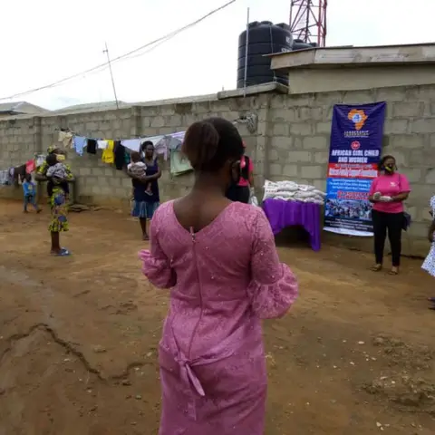 A young woman in a white t-shirt and jeans posing in front of a Leadership Foundation banner.