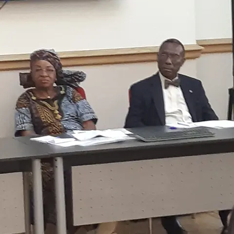 A view of a formal hall with people seated at a long table and a presenter at the side.