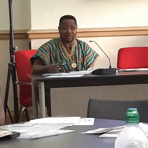 A woman in a gold sequined dress speaking into a microphone at an event.