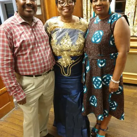 A man in a suit speaking at a formal event in a wood-paneled hall.