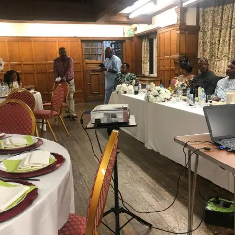 A woman standing at the front of a conference room giving a presentation.