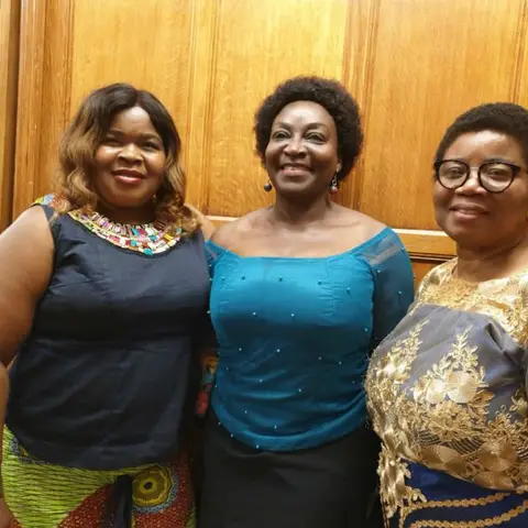 A woman in a vibrant floral dress speaking to a group of people seated in a conference room.