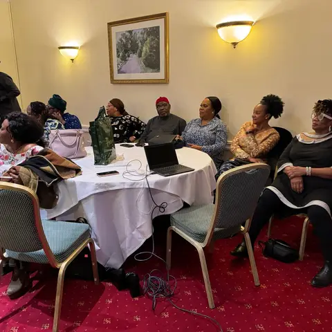 A group of women seated at a banquet table, attentively listening to the African Family Support Foundation presentation.