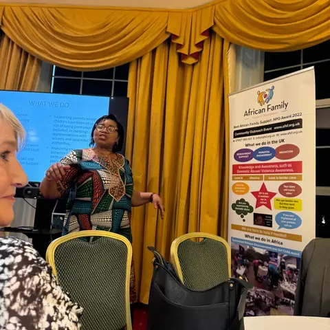 The presenter engaging with the audience during the Rotary event, standing between a 'WHAT WE DO' slide and the foundation's informational banner.