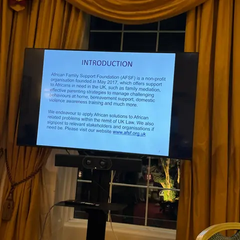 A presentation slide on a TV screen titled 'INTRODUCTION,' explaining that the African Family Support Foundation was founded in May 2017 to support Africans in the UK.