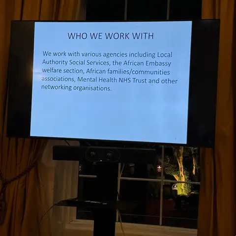 A presentation slide titled 'WHO WE WORK WITH,' listing partners like Local Authority Social Services, the African Embassy, and the NHS.