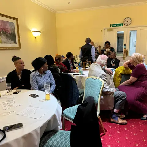 A wide shot of a banquet room with guests seated at round white-clothed tables, engaged in conversation during the Rotary event.