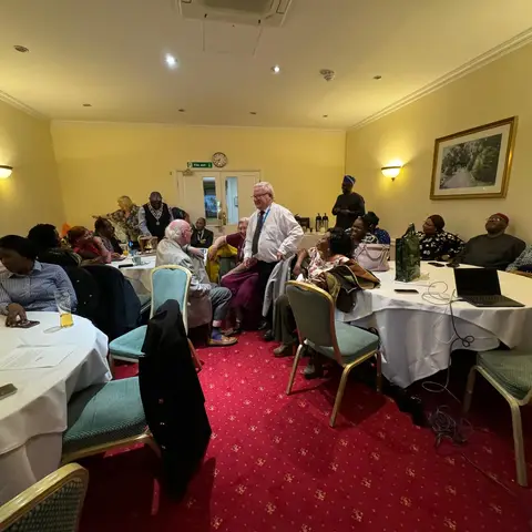 Guests and organizers interacting in a formal meeting room with yellow walls and red patterned carpet during the foundation's presentation.