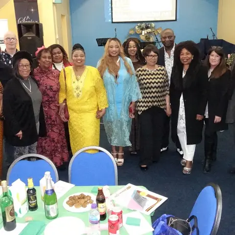 A large group of community members, volunteers, and staff posing together in a church hall next to the African Family Support Foundation banner.