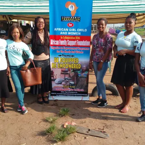Seven foundation team members and volunteers standing in front of the 'African Girl Child and Women – Be Equipped Be Empowered' banner at an outdoor event.