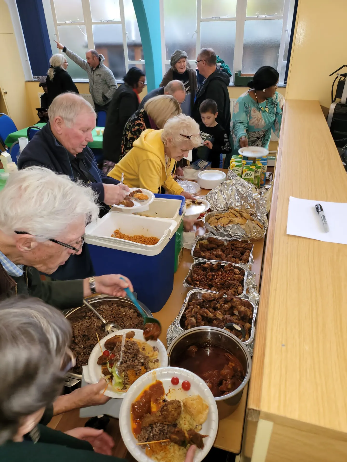 Attendees serving themselves from a buffet line featuring various dishes in large metal trays and insulated containers.